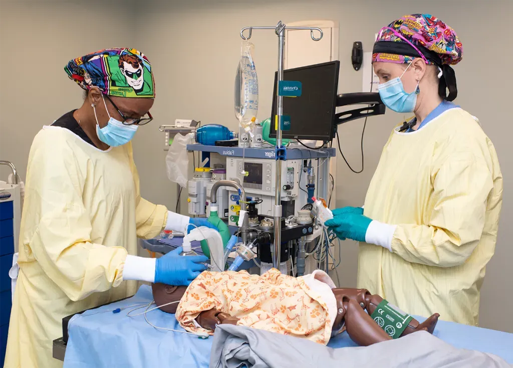 Two D.N.P. students practice giving anesthesia to a child patient simulator