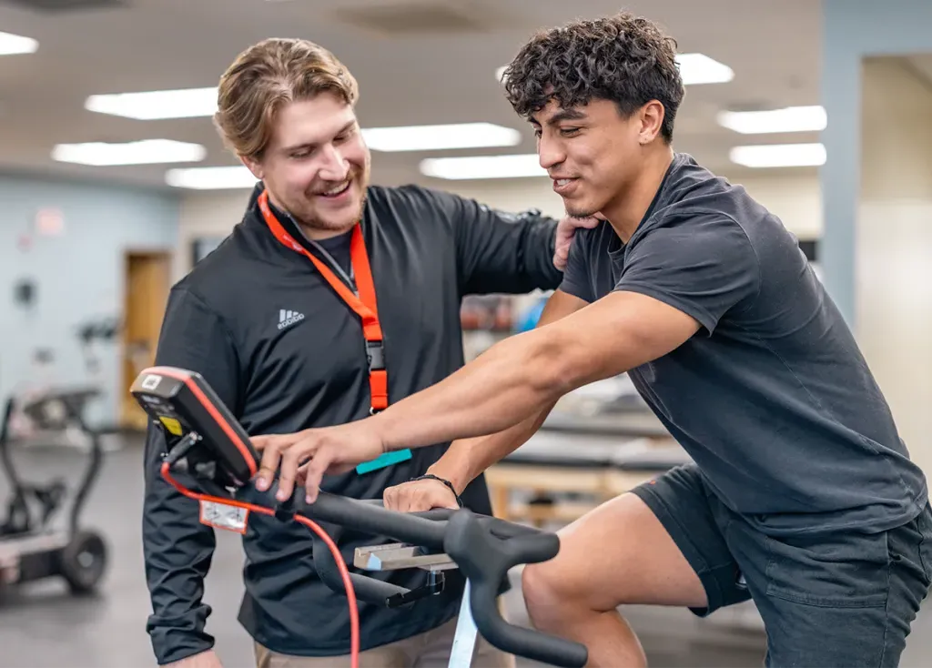 A D.P.T. student supports a patient riding a stationary bike